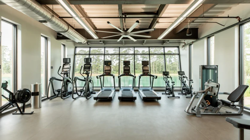Gimnasio con múltiples máquinas y ventanales con vistas al exterior